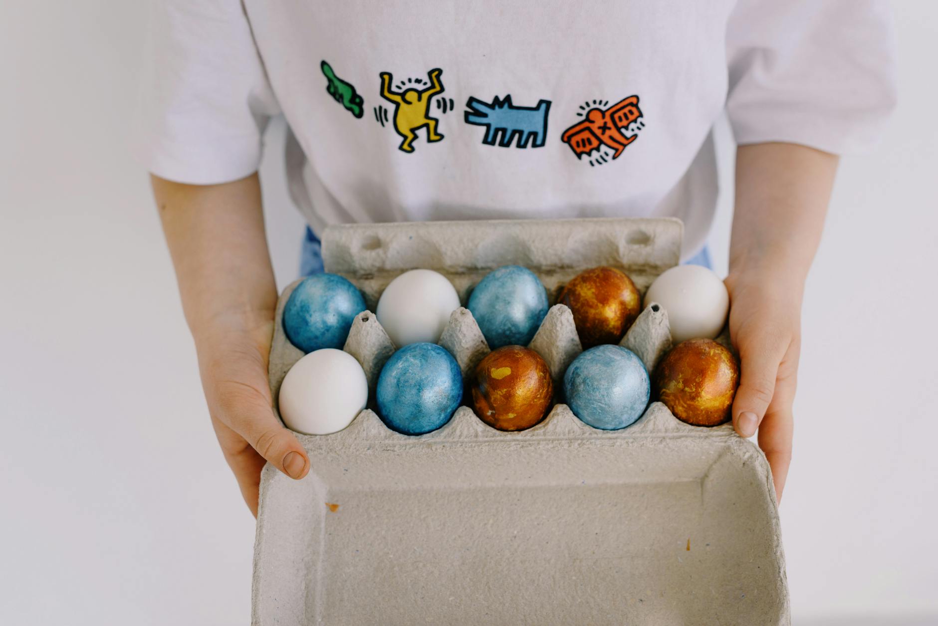 A child holding a carton filled with white and vibrant colorful Easter eggs in a casual setting.