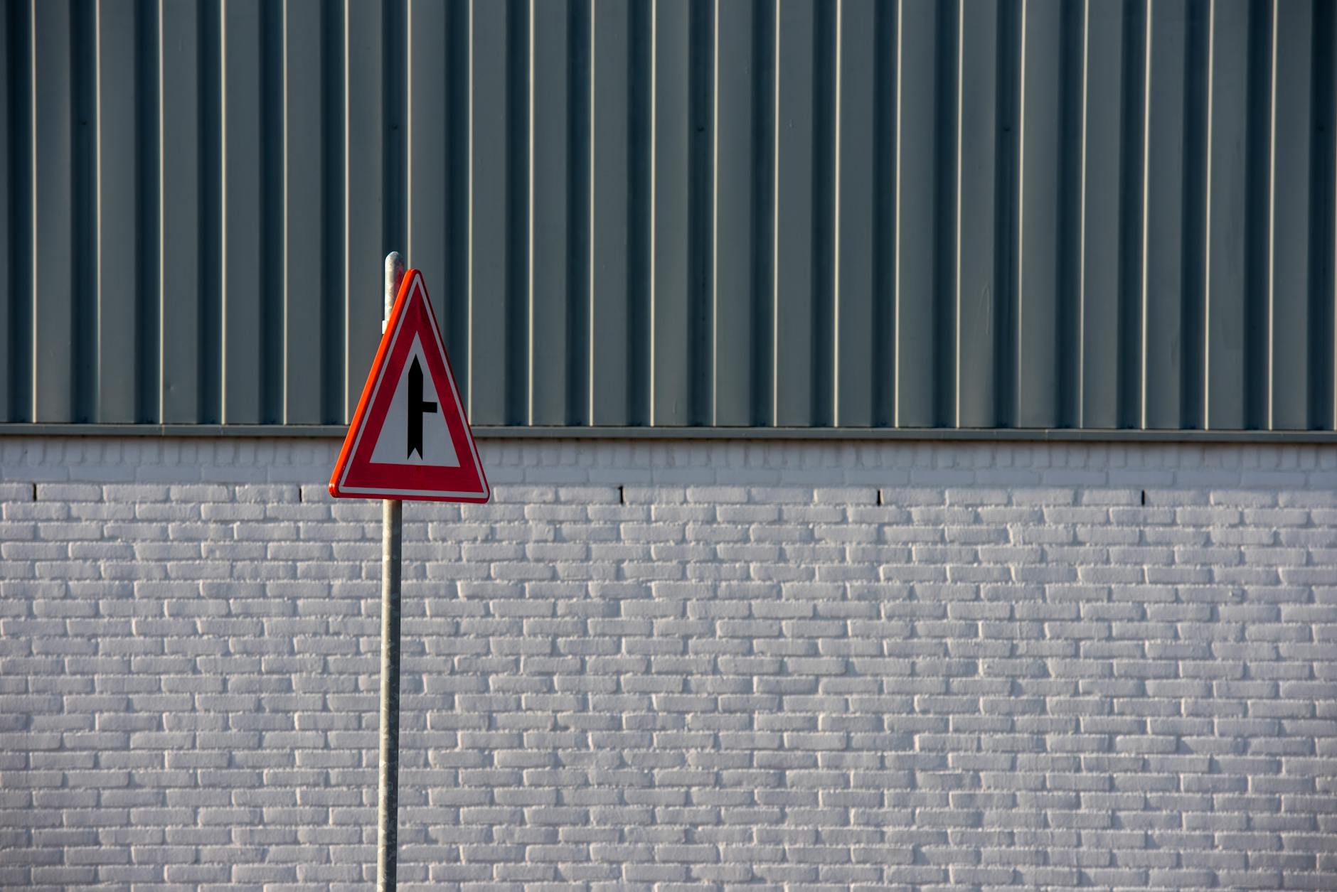 A simplistic urban traffic sign stands in front of a white brick wall and metal siding.