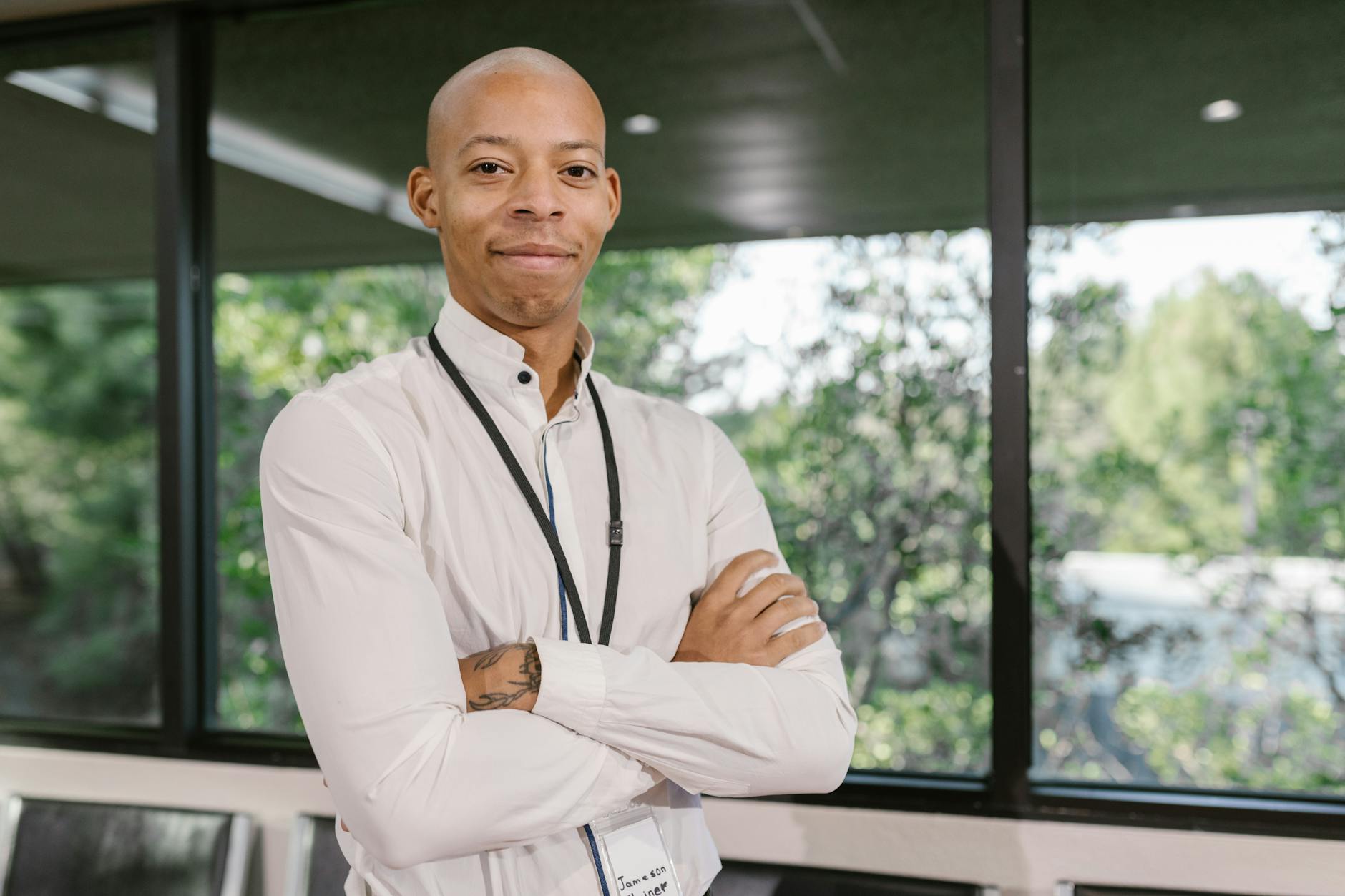 Businessman with crossed arms standing confidently indoors by a window.