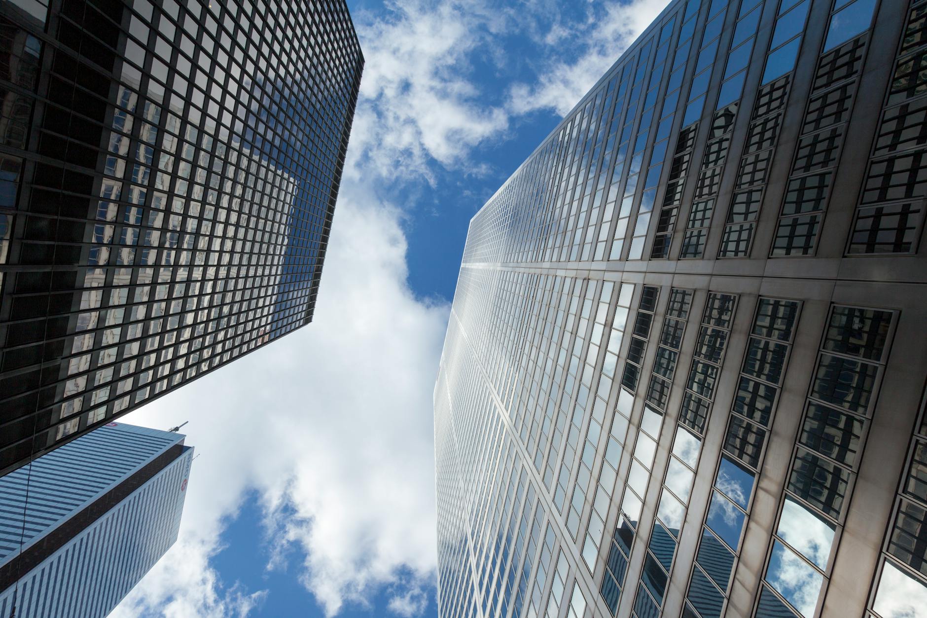 Upward view of Toronto skyscrapers reflecting the blue sky and clouds.