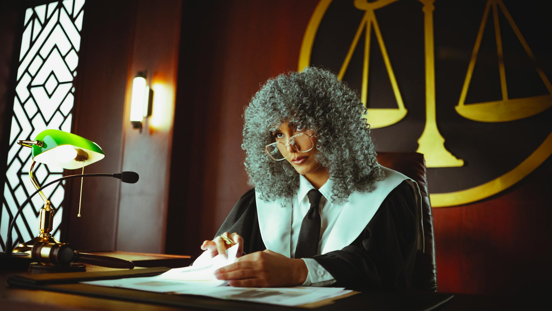 A judge in a courtroom examining documents under a classic green lamp.